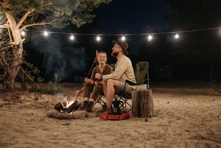 Happy couple sitting by a campfire, roasting sausages and enjoying the night outdoors.