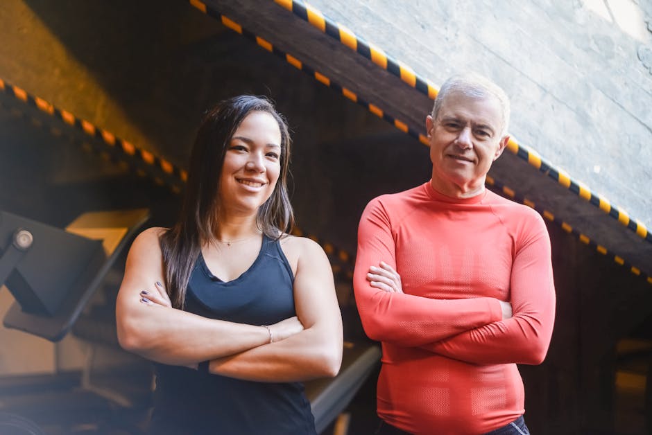 Confident man and woman standing indoors with arms crossed, exuding fitness motivation.