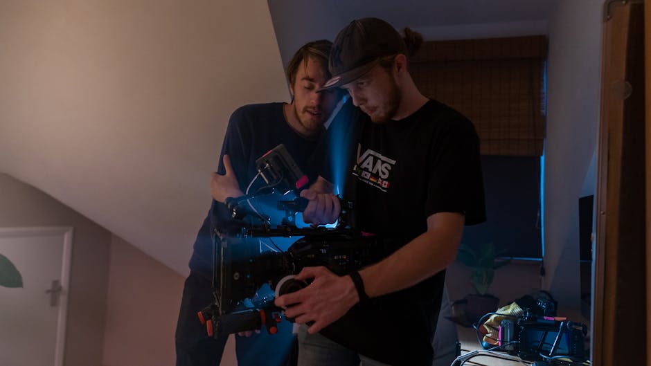 Two filmmakers setting up a camera on an indoor film set, showcasing teamwork and technology.