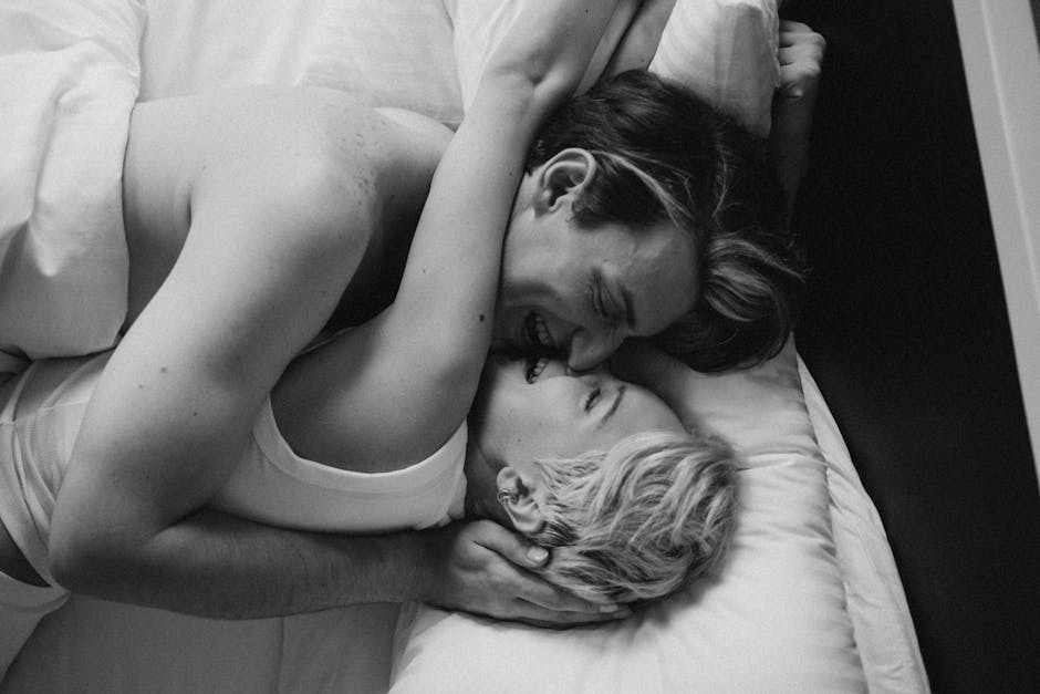 A romantic black and white photo capturing a couple's intimate embrace in bed, highlighting love and connection.