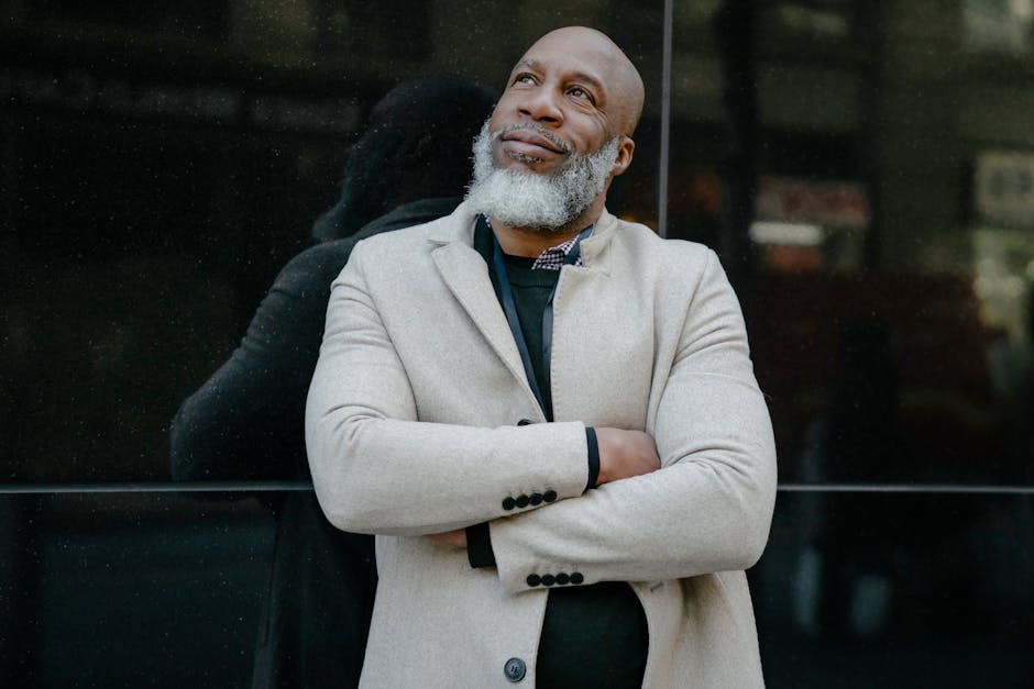 Mature man smiling confidently while leaning against a reflective surface in an urban setting.
