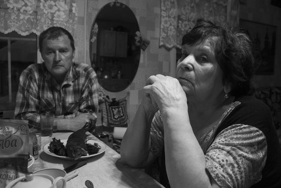 Black and white photo of a couple sitting at a dining table indoors.
