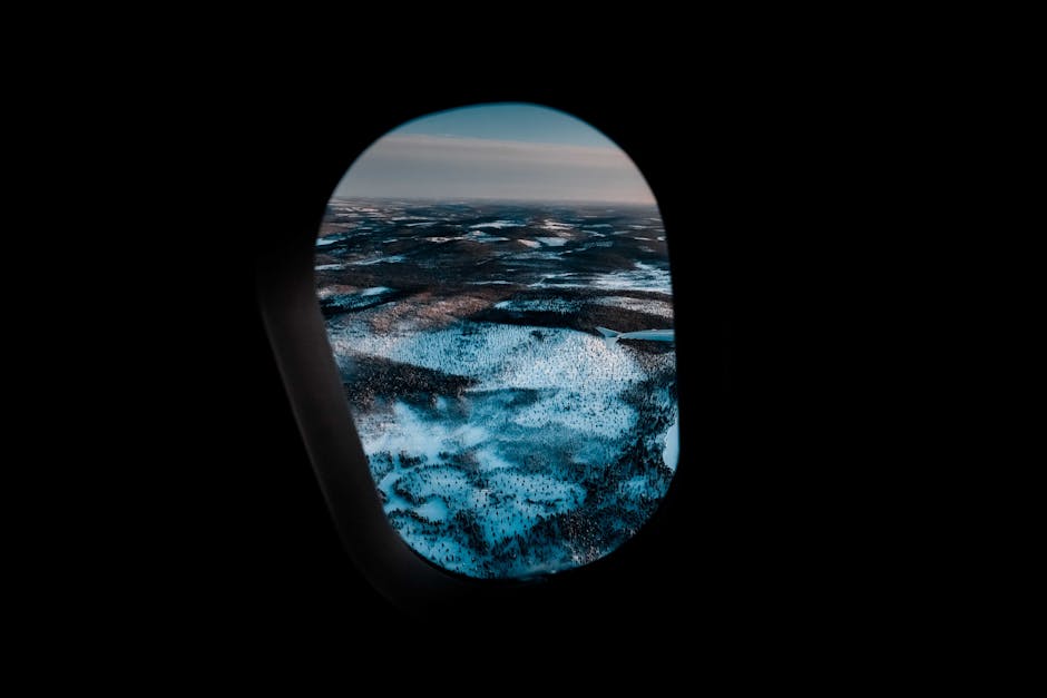 Through aircraft window of picturesque mountainous valley covered with snow under cloudy sunset sky