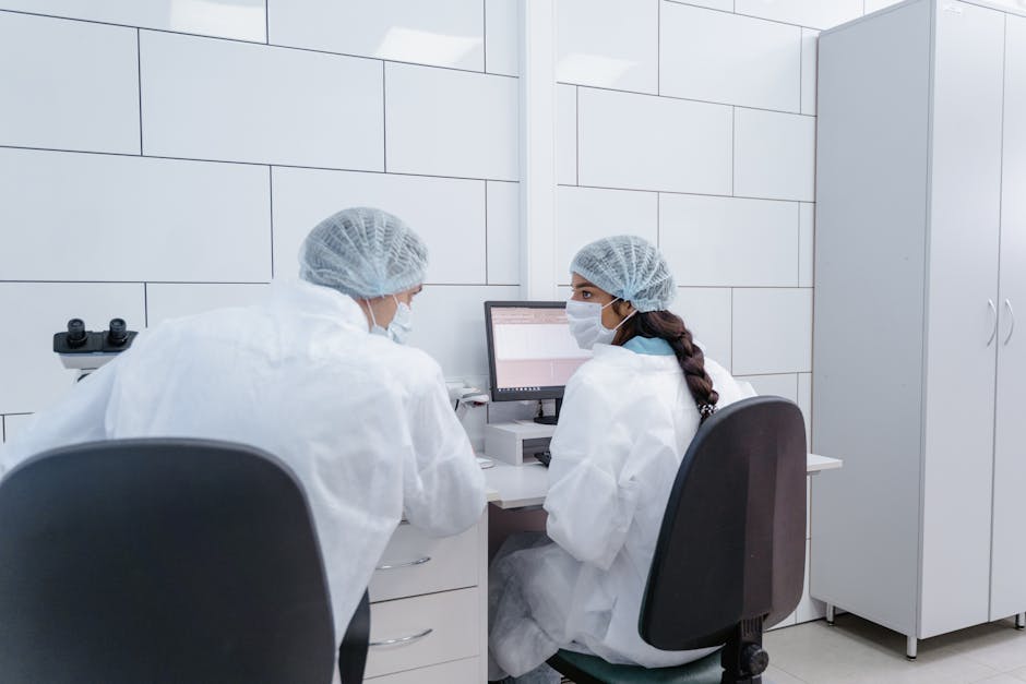 Two scientists in PPE discussing research at a computer in a laboratory setting.