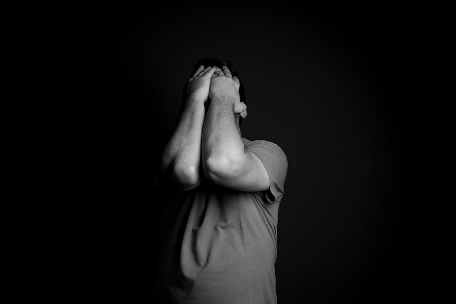A man in a t-shirt covers his face with both hands, conveying deep emotion and distress.