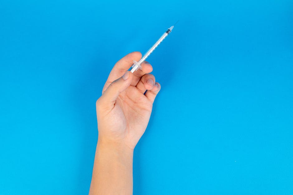 Close-up of a hand holding a syringe on a bright blue background, ideal for medical themes.