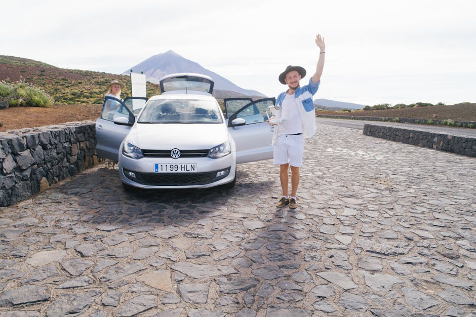 Cheerful male in white clothes standing on cobblestone near car and greeting friend while resting with wife in countryside